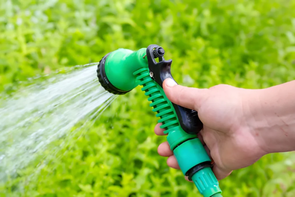 Close up of a hand holding a green garden sprayer for watering plants